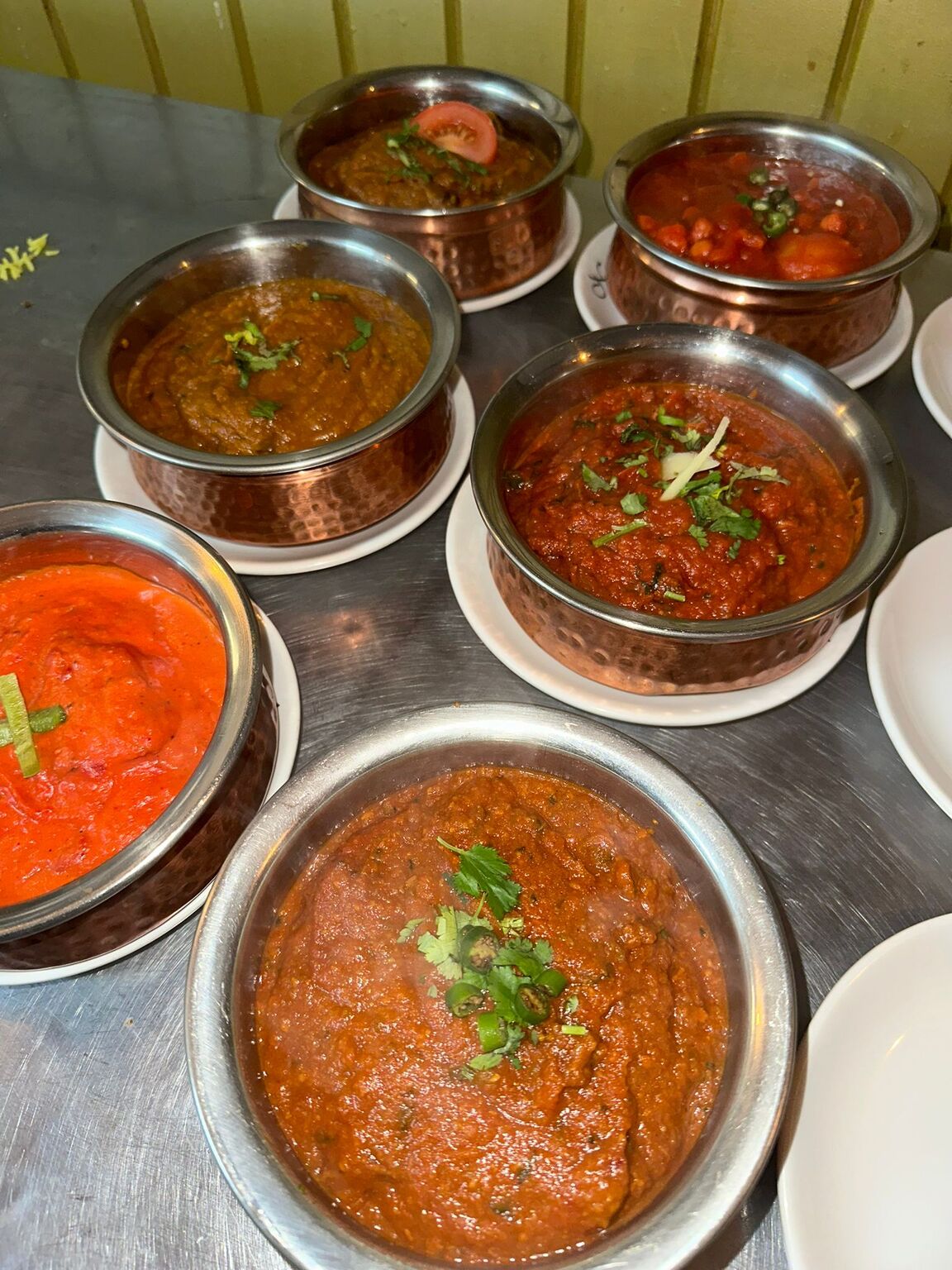 An overhead view of various colourful Indian curries served in traditional metal 
bowls at MariGold restaurant, Kilmacolm. 