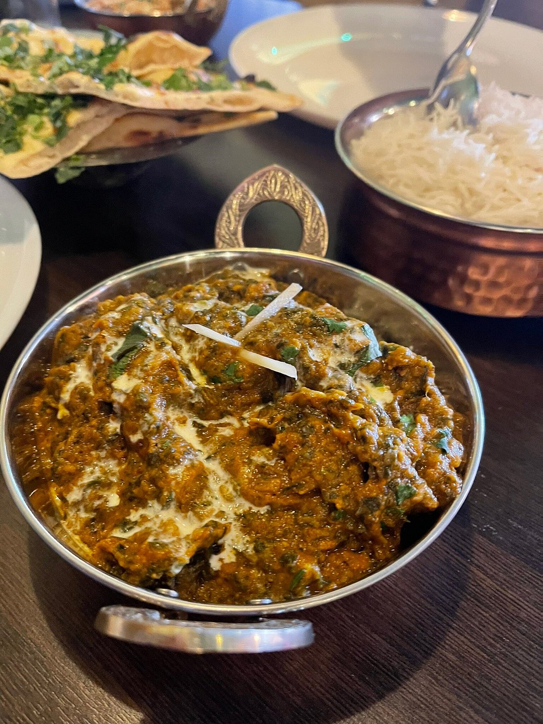 A thick spinach-based saag curry garnished with fresh cream and ginger, 
served in a traditional balti dish at MariGold restaurant in Kilmacolm 